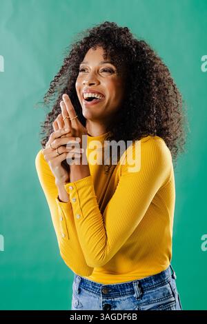 Lächelnde Frau in gelbem Pullover, die vor grünem Hintergrund einen freudigen Moment genießt. Weiblich, glücklich, Mode, stilvoll, fröhlich, positiv Stockfoto