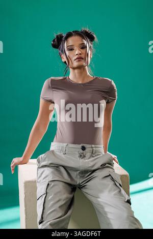 Junge Frau in lässigem Outfit posiert selbstbewusst vor leuchtend grünem Hintergrund. Mode, Selbstvertrauen, Lifestyle, bunt, trendy, fröhlich Stockfoto