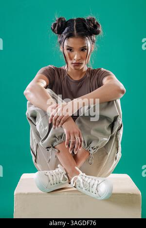 Junge Frau in lässigem Outfit, die auf einem Würfel sitzt und Grunge-Mode annimmt. Trendy, alternative, trendige, urbane, Streetwear Stockfoto