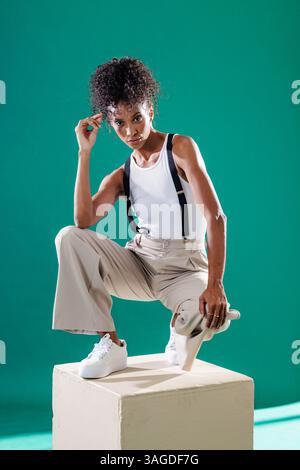 Selbstbewusste Frau in stilvollem Outfit posiert mit Skateboard in einem modernen Studio. Mode, Lifestyle, Selbstvertrauen, Bekleidung, Urban, Sport Stockfoto