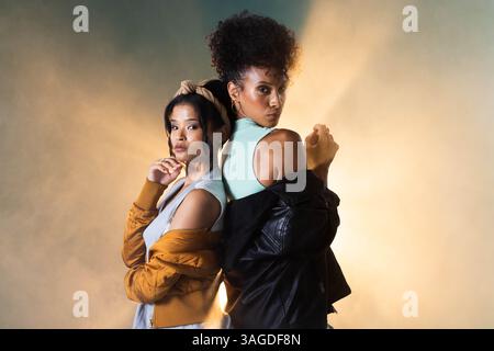Selbstbewusste Frauen, die sich Rücken an Rücken in stylischer Grunge-Mode und ausdrucksvoller Attitüde präsentieren. Style, trendy, trendig, Urban Stockfoto