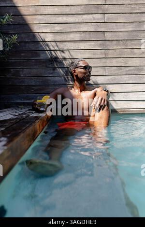 Entspannen Sie sich im Pool, Afroamerikaner genießen Drinks und Sonnenschein. Urlaub, Freizeit, Entspannung, Getränke, Luxus, am Pool Stockfoto