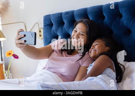 Mutter und Tochter lächeln, machen Selfie zusammen, während sie sich im Bett entspannen. Familie, Bindung, Entspannung, Technologie, Glück, Freizeit Stockfoto