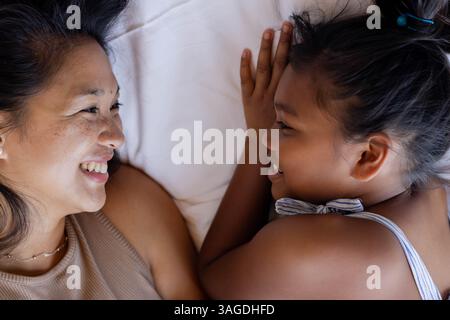 Mutter und Tochter liegen auf dem Bett, teilen ein Lächeln und genießen eine schöne Zeit. Familie, Bindung, Liebe, Zweisamkeit, Zärtlichkeit, Glück Stockfoto