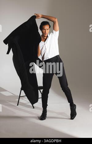 Selbstbewusster Mann in stilvollem Outfit posiert mit Jacke in modernem Studio. Mode, Stil, Selbstvertrauen, männlich, Porträt, trendig Stockfoto