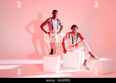 Selbstbewusste Männer posieren in stilvollen Outfits auf weißen Würfeln in einem modernen Studio. Mode, Selbstvertrauen, Style, Herrenmode, trendy Stockfoto