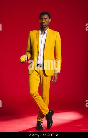 Selbstbewusster Mann in gelbem Anzug, der Zitrone hält und stilvoll im Studio posiert. Mode, lebhaft, Obst, männlich, trendy, Hochformat Stockfoto
