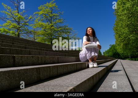 Eine ruhige Frau von Gen Z sitzt auf Betontreppen und genießt das Frühlingssonnenlicht Stockfoto