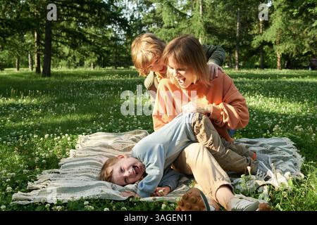Mutter mit zwei Kindern lacht auf der Decke im Park Stockfoto
