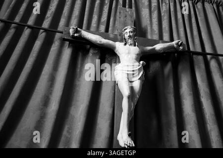 Altes hölzernes Kruzifix von Jesus Christus isoliert auf Vorhängen in der mittelalterlichen Kirche. Schwarzweißes historisches Foto. Stockfoto