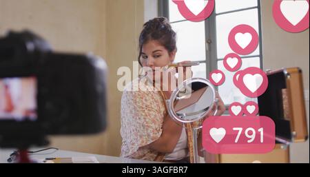 Bild von Liebessymbolen über weiblichen Make-up-Vloggern, die Vlog zu Hause aufzeichnen Stockfoto