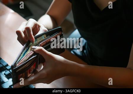 Eine Person, die ihre Geldbörse überprüft und verschiedene Karten und Bargeld darin enthüllt. Die Einstellung scheint ein Schreibtisch mit einem Laptop im Hintergrund zu sein, was andeutet Stockfoto