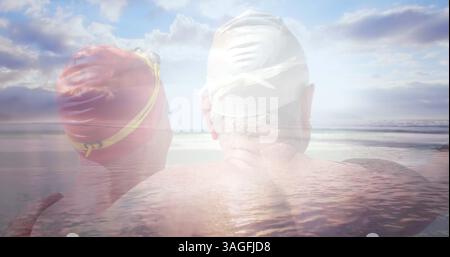 Bild von leuchtendem Licht über glücklichem Seniorenpaar in Badehüten am Meer Stockfoto