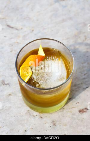 Über dem Blick auf einen Whiskey-Cocktail mit einem großen Eiswürfel, dekoriert mit einer Orangenschale auf einer Tischplatte aus bege-Marmor Stockfoto