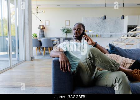 Zu Hause entspannen, Afroamerikaner, der auf dem Sofa sitzt und auf dem Smartphone spricht. Technologie, Kommunikation, Lifestyle, Konversation, Freizeit, entspannen Sie sich Stockfoto