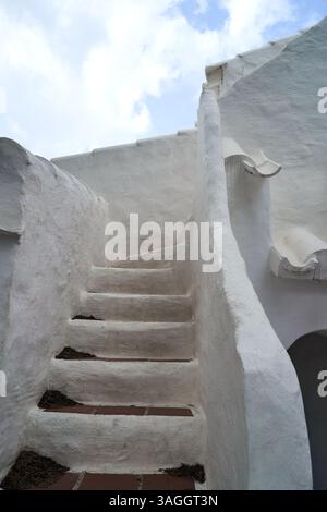 Ein bezaubernder Blick auf die weiße Treppe in Binibeca, Menorca, die vor dem Hintergrund eines blauen Himmels nach oben führt. Die Architektur zeichnet sich durch ein einzigartiges Design aus. Stockfoto