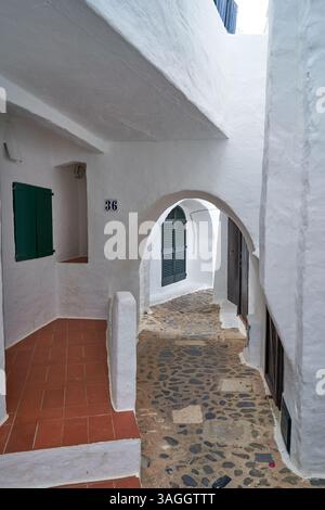 Ein malerischer Blick auf eine enge Binibeca-Straße mit traditioneller weiß getünchter Architektur mit Bogengängen und Fensterläden. Stockfoto