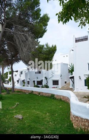Binibeca, Menorca: Ein bezaubernder Blick auf weiß getünchte Gebäude, üppiges grünes Gras und eine Steinmauer, die die einzigartige Architektur zeigt. Stockfoto