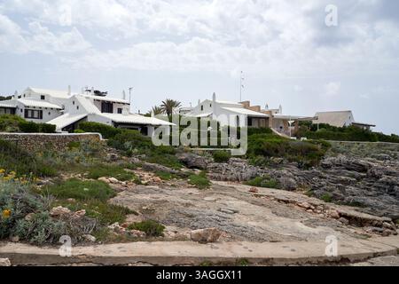 Malerischer Blick auf weiß getünchte Villen in Binibeca, Menorca, Spanien. Die Architektur ist charakteristisch für die Balearen mit üppigem Grün und Wolken Stockfoto