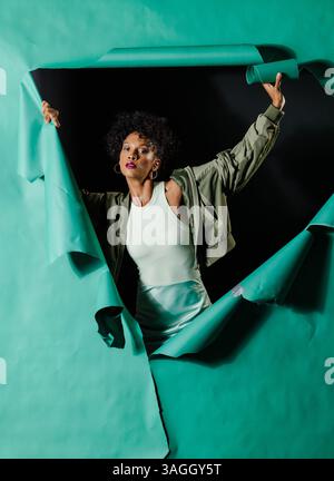 Die Afroamerikanerin bricht durch den Hintergrund des Papiers und zeigt Entschlossenheit und Stärke. Empowerment, Durchbruch, Macht, Resilienz, Vertrauen, Stockfoto