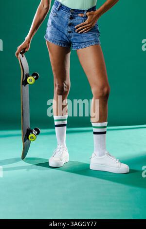 Person mit Skateboard in Jeansshorts und Sneakers, bereit für Action. Skateboarding, Lifestyle, Streetwear, Urban, Freizeit, aktiv Stockfoto