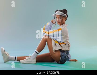 Asiatische Frau in lässigem Outfit sitzt auf dem Boden und blickt nachdenklich in die Kamera. Kontemplation, Lifestyle, Entspannung, Denken, drinnen, Hochformat Stockfoto