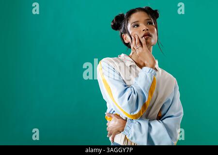 Nachdenkliche junge Frau in stilvoller Jacke posiert vor grünem Hintergrund. Mode, Porträt, Kontemplation, Stil, Eleganz, selbstbewusst Stockfoto
