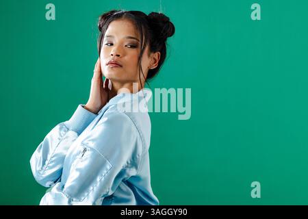 Selbstbewusste junge Frau in blauer Jacke posiert vor grünem Hintergrund. Mode, Stil, Porträt, Selbstvertrauen, trendy, lebendig Stockfoto
