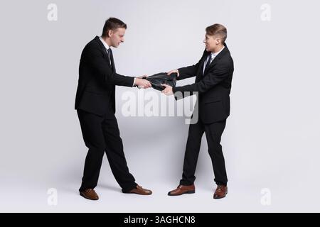 Wettbewerbskonzept. Geschäftsleute ziehen Lederaktentasche auf grauem Hintergrund Stockfoto