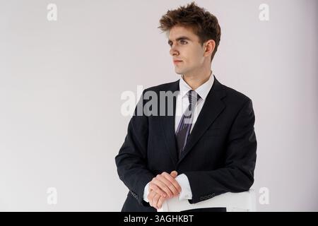 Porträt eines jungen Geschäftsmannes in einem dunklen karierten Anzug mit einer lila Krawatte, der vor einem hellgrauen Hintergrund nachdenklich zur Seite blickt. Stockfoto