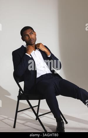 Selbstbewusster Mann in stilvollem Anzug, der den Kragen verstellt, während er auf dem Stuhl sitzt. Mode, Selbstvertrauen, Business, Eleganz, Formalwear, Herrenbekleidung Stockfoto