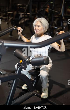 Ältere Frau, die im Fitnessstudio auf einem Lat Pulldown-Gerät trainiert Stockfoto