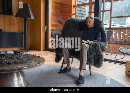 Mann, der an einem Laptop in einem luxuriösen Chalet in den italienischen Alpen arbeitet Stockfoto