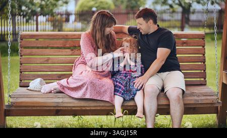 Familie genießt sonnigen Hinterhof-Moment, Eltern und Kind verbinden sich auf Holzschaukel, teilen warme Verbindung und Glück Stockfoto