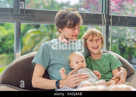 Vater, Sohn und neugeborenes Baby sitzen auf der Couch und feiern freudig die neueste Ergänzung ihrer Familie. Elternschaft, Bindung und Familienliebe Stockfoto