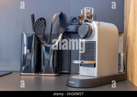 Kompakte und stilvolle Kaffeeecke mit Krups Nespresso-Maschine, Küchenutensilien und Kapselhalter vor einem eleganten dunklen Hintergrund. Stockfoto