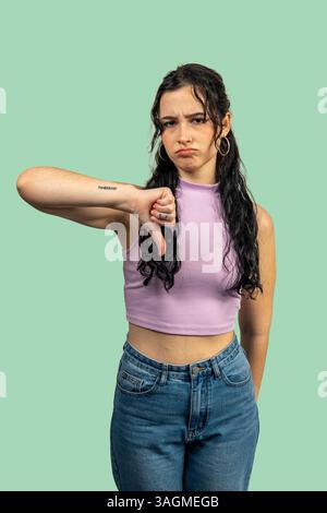 Junge Frau mit Daumen nach unten Geste, Missbilligung und negatives Feedback auf grünem Hintergrund Stockfoto