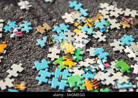 Ein Hintergrundbild von einem Stapel von gemischten, bunten Puzzle-Stücken, die auf dem grauen Asphaltpflaster auf der Straße verstreut sind. Chaotisches Konzept. Cl Stockfoto
