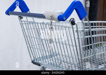 Verlassener verlassener leerer Einkaufswagen aus Metall mit blauem Griff, der im Hinterhof des Ladens an der schmutzigen Betonwand an der Kopfsteinpflasterstraße stand. Fragment, Beschneidung Stockfoto