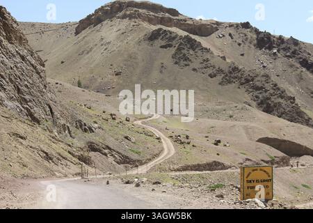 Eine unbefestigte Straße schlängelt sich durch die bergige Landschaft von Leh Ladakh, mit felsigen Hügeln und klarem blauen Himmel darüber. Stockfoto