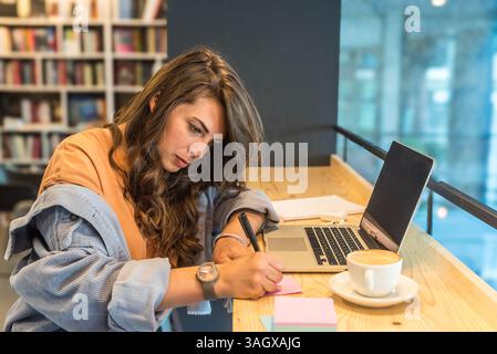 Junge freischaffende Geschäftsfrau, müde und müde von der Arbeit, die faul in der Bibliothek auf Laptop-Computer arbeitet. Gestresste und ängstliche weibliche Überlastung des Gehirns Stockfoto
