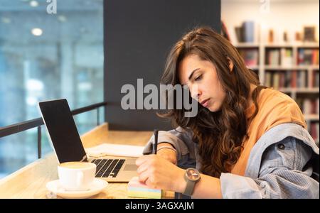 Junge freischaffende Geschäftsfrau, müde und müde von der Arbeit, die faul in der Bibliothek auf Laptop-Computer arbeitet. Gestresste und ängstliche weibliche Überlastung des Gehirns Stockfoto