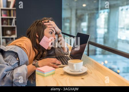 Junge freischaffende Geschäftsfrau, müde und müde von der Arbeit, die faul in der Bibliothek auf Laptop-Computer arbeitet. Gestresste und ängstliche weibliche Überlastung des Gehirns Stockfoto