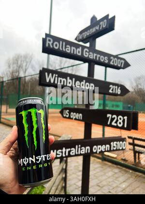 Kiew, Ukraine - 08. April 2025: Energy Drink Monster Dose gegen ein Schild mit verschiedenen Sportzielen auf dem Tennisplatz. Stockfoto