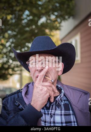 Bauer mit Hut raucht Zigarette. Porträt eines alten älteren Mannes, der eine Zigarre raucht. Ein Mann mit Cowboyhut, der eine Zigarillo raucht. Cowboy raucht eine Zigarre Stockfoto