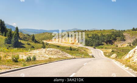 Straße in Bosnien und Herzegowina, Europa. Die malerische Straße schlängelt sich durch grüne Hügel unter einem klaren blauen Himmel und verspricht eine Reise voller Naturschönheiten Stockfoto