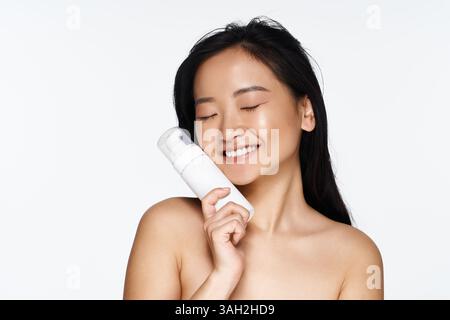 Eine junge Frau genießt ihr Hautpflegeprodukt, während sie im Haus Glück und Selbstvertrauen ausdrückt. Stockfoto