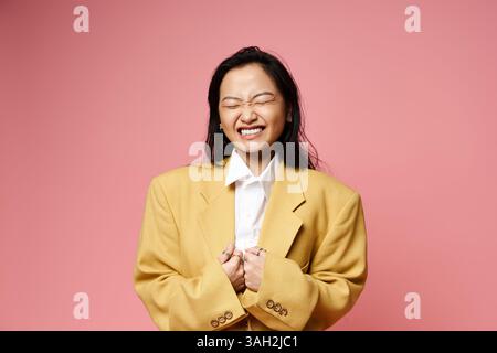 Eine junge Asiatin in einer großen gelben Jacke lächelt und spiegelt ihren verspielten Geist wider. Stockfoto