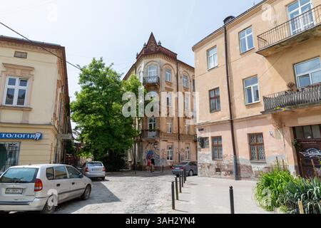 LEMBERG, UKRAINE - 20. Juni 2021: Sonnenlicht beleuchtet die bezaubernden Straßen des historischen Teils von Lemberg, mit eleganter Architektur und lebhaftem Grün, das die Kopfsteinpflaster säumt. Stockfoto
