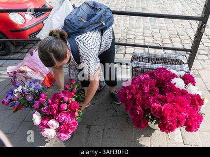 LEMBERG, UKRAINE - 20. Juni 2021: Straßenverkäufer zeigen bunte Blumenarrangements, während sie sich um ihre Stände kümmern. Die Atmosphäre ist lebhaft, wenn die Einheimischen vorbeikommen und die Blumenangebote genießen. Stockfoto